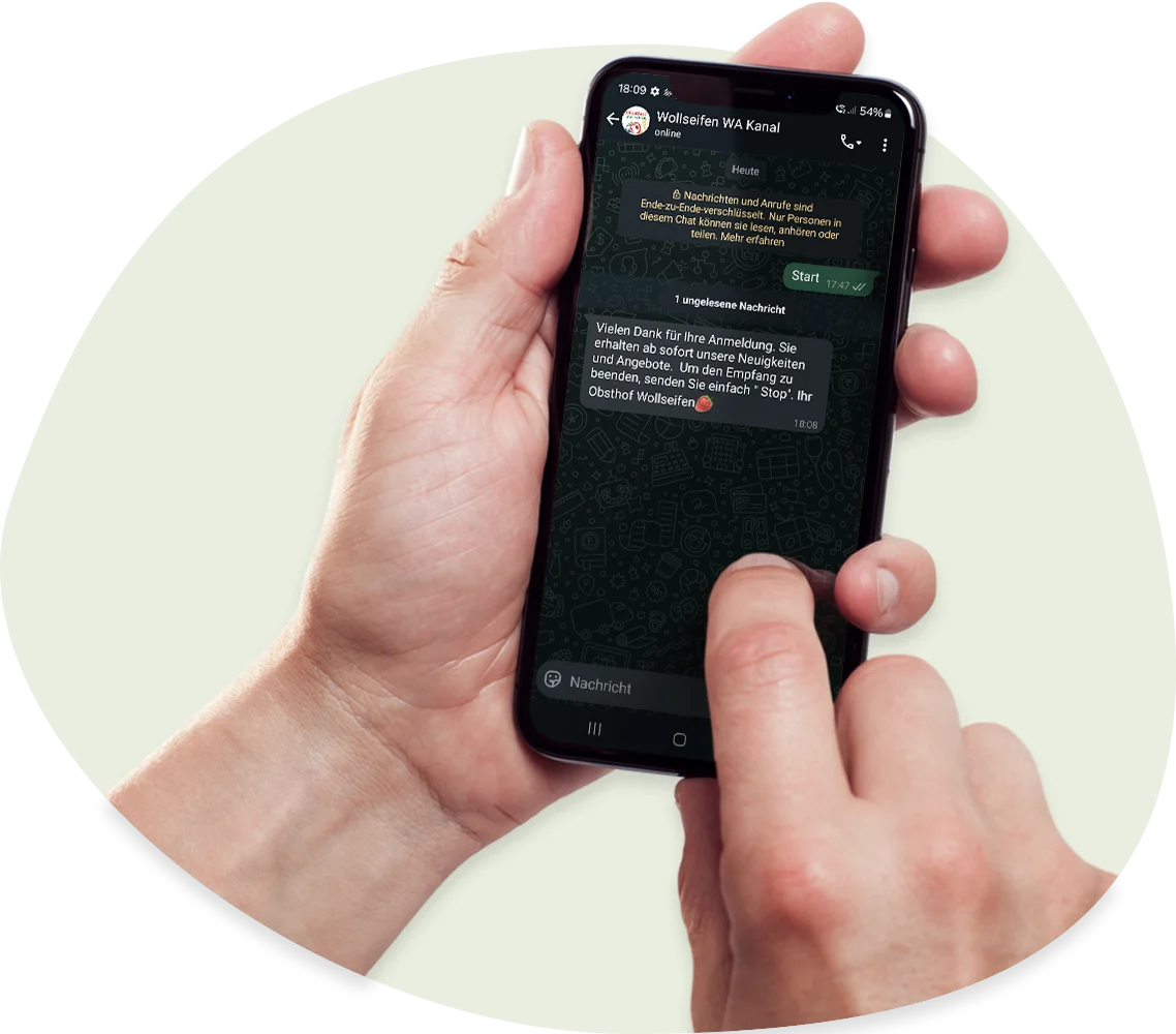 Eine Person hält ein Smartphone in der linken Hand, während sie mit dem rechten Zeigefinger durch einen WhatsApp-Chat navigiert; das Gespräch findet auf Deutsch statt und der Bildschirm des Telefons ist deutlich sichtbar.